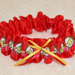 May include: Red satin garter with a yellow bow and a white and red print of the Flash logo.