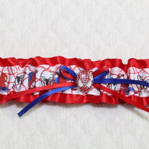 May include: Red and blue garter with a white satin base featuring a repeating pattern of Spiderman characters. A red and blue bow with a Spiderman face button is in the center.