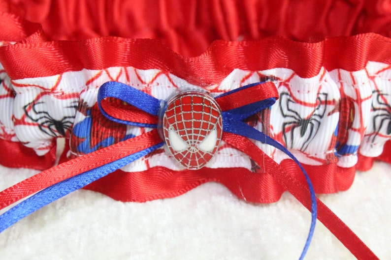 May include: Red and blue garter with a white background featuring a Spiderman design and a red and silver Spiderman head charm.
