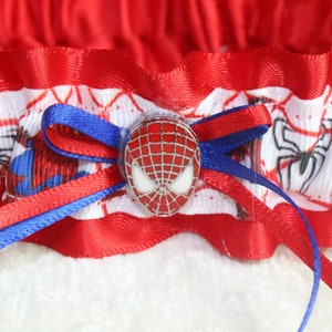 May include: Red and blue garter with a white background featuring a Spiderman design and a red and silver Spiderman head charm.