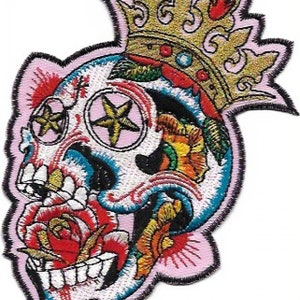 Puede incluir: Parche bordado para planchar con un cráneo de azúcar colorido con una corona, una rosa y ojos en forma de estrella. El cráneo está bordeado de negro y tiene un fondo rosa.