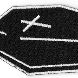 Könnte beinhalten: Schwarzer und weißer gestickter Aufnäher in Form eines Sarges mit einem weißen Kreuz darauf.
