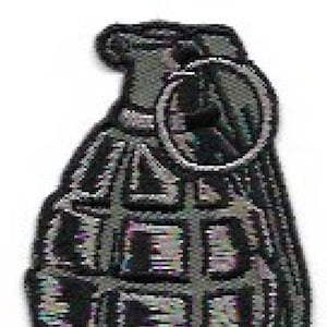 May include: A black and gray grenade-shaped patch with a textured surface. The patch has a ring on the top.