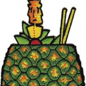 May include: A green pineapple with yellow and orange accents, topped with a yellow and orange pineapple with a red cherry on top. Two yellow chopsticks are sticking out of the top of the pineapple.