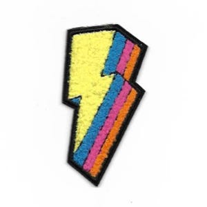 May include: A yellow lightning bolt with orange, pink, and blue stripes. The lightning bolt is outlined in black and has a fuzzy texture.