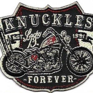 Pode incluir: Patch bordado com um design de motocicleta. O patch é preto com detalhes em branco e vermelho. O texto inclui "KNUCKLES", "Lucky 13", "EST. 1991" e "FOREVER". O patch tem formato de escudo com uma borda decorativa.