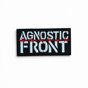 May include: A rectangular embroidered patch with a black background and white text that reads AGNOSTIC FRONT. A thin red line resembling barbed wire runs horizontally across the center of the patch, intersecting the letters of the text.