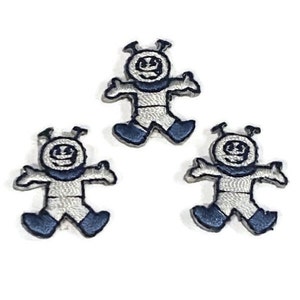 May include: Three white embroidered iron-on patches of a cartoon astronaut with a smiling face and blue accents.