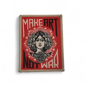 May include: A rectangular patch with a red background, featuring the text "MAKE ART NOT WAR" in black and white. The design includes a central illustration of a woman's face, laurel wreath, and decorative elements.