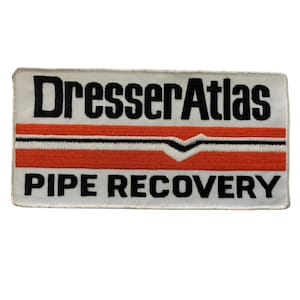 May include: White embroidered patch with black text that reads "Dresser Atlas Pipe Recovery". The patch has a red and white stripe with a black chevron.