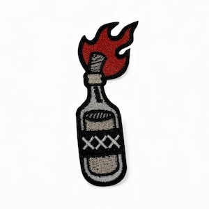 Op de afbeelding: Geborduurde patch met een fles met een rode vlam. De fles is grijs met zwarte details en de tekst "XXX". De patch is zwart omlijnd en geschikt voor kleding of stoffen artikelen.