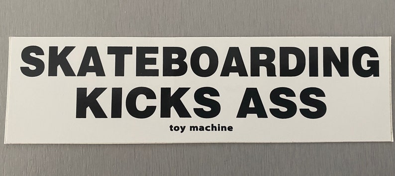 Może przedstawiać: Biała naklejka z czarnym tekstem, kt&oacute;ry brzmi "Skateboarding Kicks Ass" i "toy machine" mniejszą czcionką.