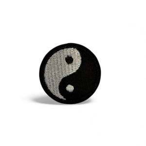 以下が含まれることがあります： 陰陽のシンボルをあしらった、丸い刺繍パッチ。デザインは2つの半分に分かれています。黒い背景に白い曲線、白い背景に黒い曲線。パッチは白い背景にあります。