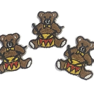 Op de afbeelding: Drie geborduurde teddybeer-patches in bruin met gele en rode trommels en zwarte drumsticks. De beren dragen bruine vlinderdasjes.