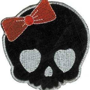 May include: Black skull patch with white heart-shaped eyes and a small nose. A red bow is stitched on the top left. The patch has a white border.