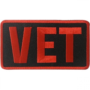 Puede incluir: Parche bordado rojo con la palabra "VET" en letras negras delineadas.