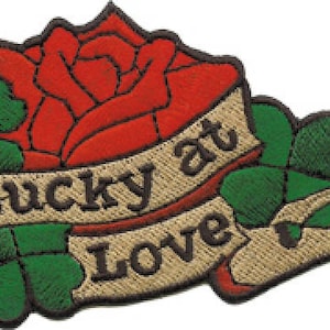 May include: Embroidered patch with a red rose, green shamrocks, and a banner that reads "Lucky at Love".