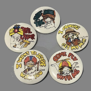 May include: Five round pins with colorful cartoon characters and sayings. The pins say "Sweet Thing", "Real Charmer", "I Always Get My Man", "I Want To Score With You", and "Come Fly With Me".
