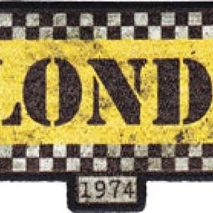 Op de afbeelding: Een geel en zwart geruit bord met het woord "BLONDIE" in zwarte letters en het jaar "1974" in zwarte letters eronder.