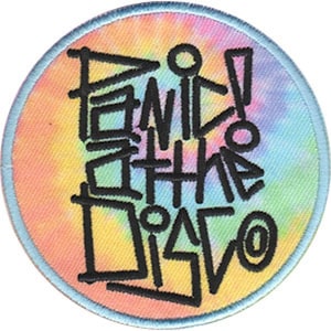 May include: Circular patch featuring the text "Panic! At The Disco" in black, graffiti-style lettering. The background is a tie-dye pattern with shades of yellow, orange, pink, purple, and blue. It has a light blue border.