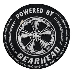 May include: Black and white embroidered patch with a tyre rim design and the text "Powered by Gearhead".