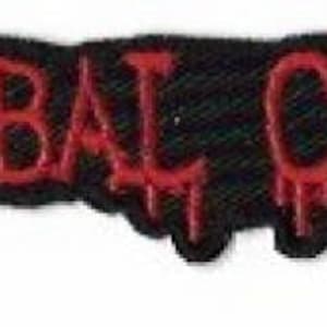 May include: A rectangular embroidered patch featuring the text CANNIBAL CORPSE in a stylized, dripping red font against a solid black background. The lettering has a distinct, jagged appearance with red drips extending downward from the characters.
