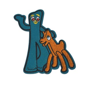 May include: Embroidered patch depicting the cartoon characters Gumby and Pokey. Gumby is teal with a yellow smile and red eyes, and Pokey is orange. The patch has a black border and is designed for clothing or accessories.