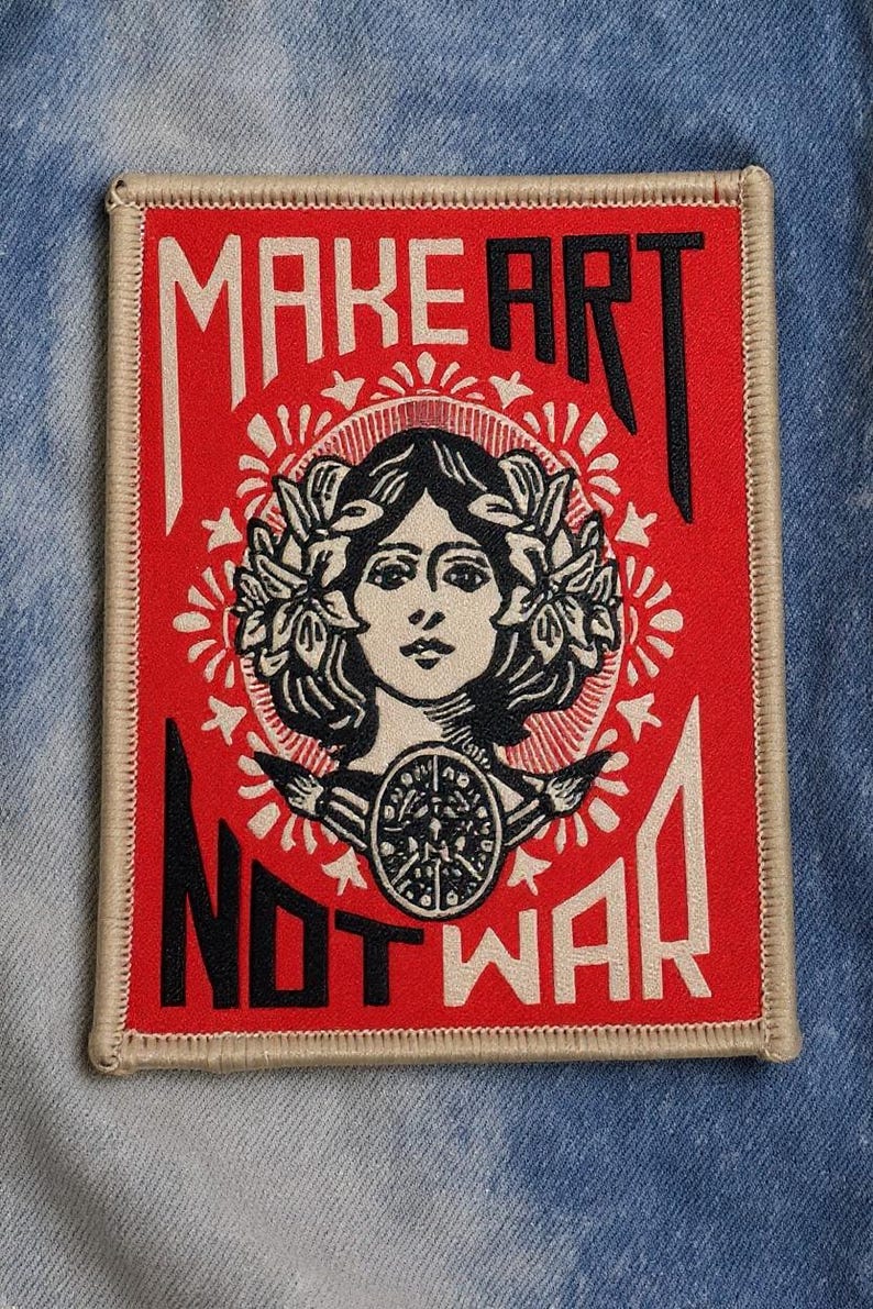 May include: Embroidered patch with a red background and the text "MAKE ART NOT WAR" in white and black. The patch features a woman's face with a laurel wreath and a circular design.