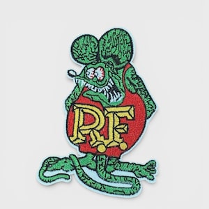 Op de afbeelding: Geborduurde patch met een cartoon rat karakter in groen en rood. De rat heeft grote oren, een grijnzende grijns en draagt een rood tanktop met de gele letters "RF". De patch heeft een lichtblauwe rand.