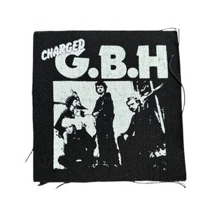 May include: Black square patch with the text "CHARGED G.B.H" in white. The patch features a black and white graphic of three figures. The patch is made of a woven fabric.