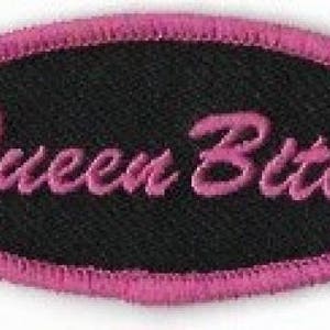 May include: Pink oval-shaped patch with black fabric and the text "Queen Bitch" in pink lettering.