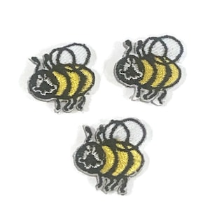 Może przedstawiać: Trzy haftowane naszywki do prasowania w kształcie żółto-czarnych trzmieli z białymi skrzydłami.