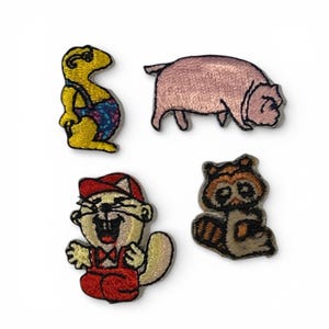 Op de afbeelding: Vier geborduurde patches met cartoon dieren. Inclusief een geel wezen met blauwe en paarse tuinbroek, een roze varken, een bever met een rode pet en overall, en een wasbeer. Geschikt voor kleding of accessoires.