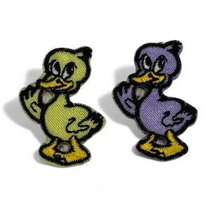 Puede incluir: Dos parches bordados para planchar de patos de dibujos animados. Un pato es amarillo y el otro es morado.