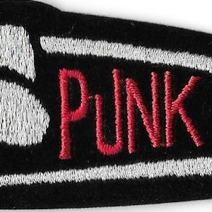 May include: Black embroidered patch in the shape of a safety pin. The word "PUNK" is embroidered in red, with the pin's outline in white. The patch is designed for clothing or accessories.