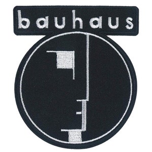 Puede incluir: Parche negro con la palabra "bauhaus" bordada en blanco sobre un diseño circular. El diseño presenta un contorno blanco y formas geométricas, incluyendo un cuadrado y líneas verticales, sobre un fondo negro.