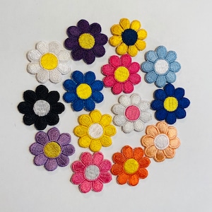 Peut inclure: Assortiment de 13 patchs de fleurs en feutre de couleurs différentes, chacune avec un centre jaune et une couche extérieure de couleur différente. Les fleurs sont disposées en cercle sur un fond blanc.