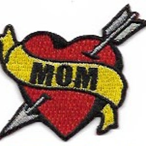 Puede incluir: Corazón rojo con una flecha que lo atraviesa y una pancarta amarilla que dice "MOM".