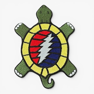 May include: Embroidered turtle-shaped patch. The green turtle has a yellow shell with a red, blue, and white lightning bolt design. This patch is designed to be sewn onto clothing or accessories.