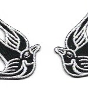May include: Two black and white embroidered swallow bird patches. The birds are facing opposite directions and have a traditional tattoo style.