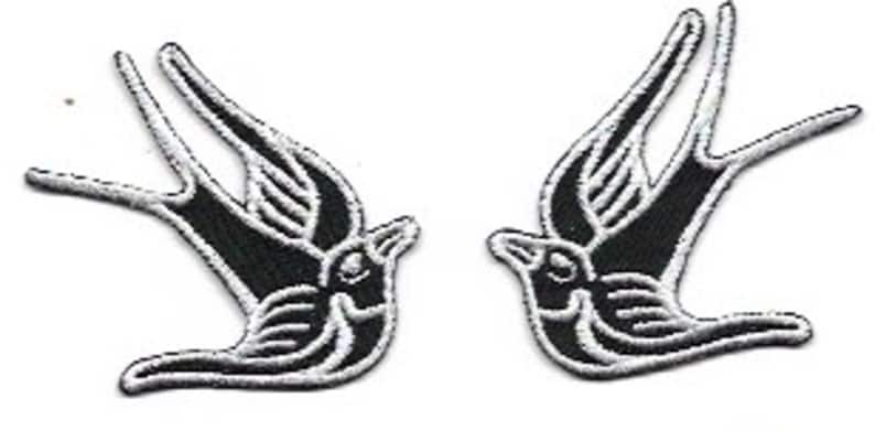 May include: Two black and white embroidered swallow bird patches. The birds are facing opposite directions and have a traditional tattoo style.