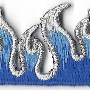 Könnte beinhalten: Gestickter Aufnäher mit einem blauen Flammen-Design und silbernen Konturen. Die Flammen haben einen Farbverlauf, der von einem helleren Blau zu einem dunkleren Farbton übergeht. Zum Aufnähen auf Stoff.