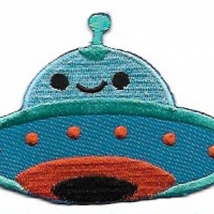 May include: A blue and orange embroidered patch in the shape of a cartoon UFO. The UFO has a smiling face, orange dots, and a teal outline. The patch is designed for decorative purposes, such as on clothing or bags.