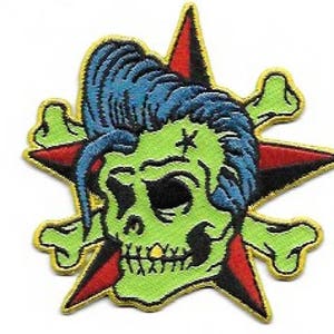 May include: Embroidered patch featuring a green zombie skull with blue hair, a gold tooth, and a star-shaped background with red and black accents. The design includes crossed bones and a yellow border.