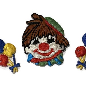 Peut inclure: Ensemble de patchs brodés à repasser représentant un clown souriant avec des cheveux bruns et un chapeau vert, ainsi que deux ensembles de ballons colorés.