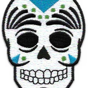 May include: White sugar skull with black eyes, a black nose, and a black mouth. The skull has a blue and green design on the forehead and cheeks.