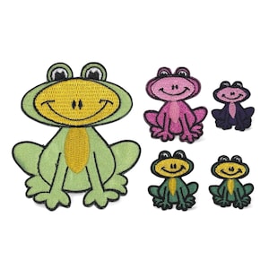 Op de afbeelding: Een verzameling geborduurde kikkerpatches in verschillende kleuren. De patches hebben lachende kikkerontwerpen in groen, roze en paars. De kikkers hebben zwarte ogen en gele buiken, perfect om toe te voegen aan kleding of accessoires.