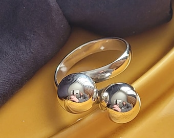 May include: A silver ring with two round balls on the band. The balls are smooth and reflective.