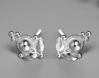 May include: A pair of silver stud earrings with a delicate, intricate design featuring a central bead and small, rounded accents.