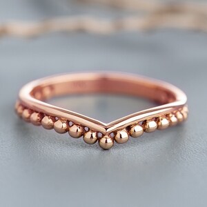 May include: A rose gold ring with a V-shaped band and a row of small beads along the edge.